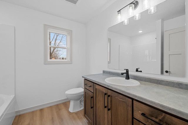 bathroom with baseboards, toilet, wood finished floors, vanity, and a bath