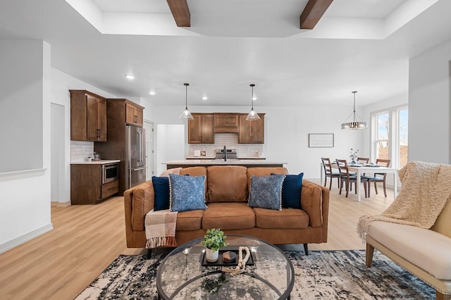 living room featuring beam ceiling, sink, an inviting chandelier, and light wood-type flooring