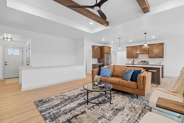 living room with sink, light hardwood / wood-style flooring, beamed ceiling, and ceiling fan