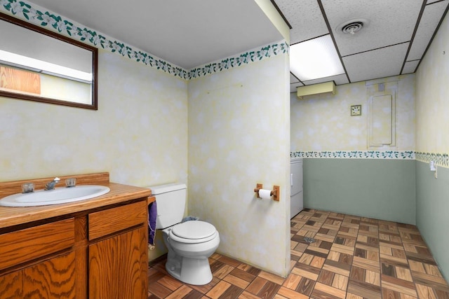 bathroom featuring toilet, parquet floors, vanity, washer / clothes dryer, and a drop ceiling