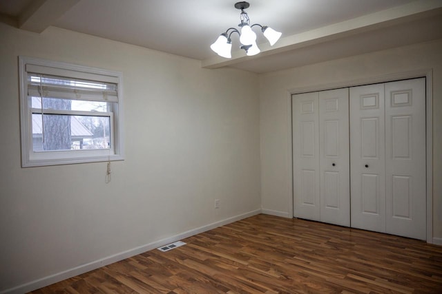 unfurnished bedroom featuring dark hardwood / wood-style floors, a closet, and a notable chandelier