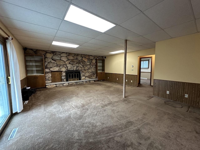 basement featuring wood walls, a fireplace, carpet, and a drop ceiling