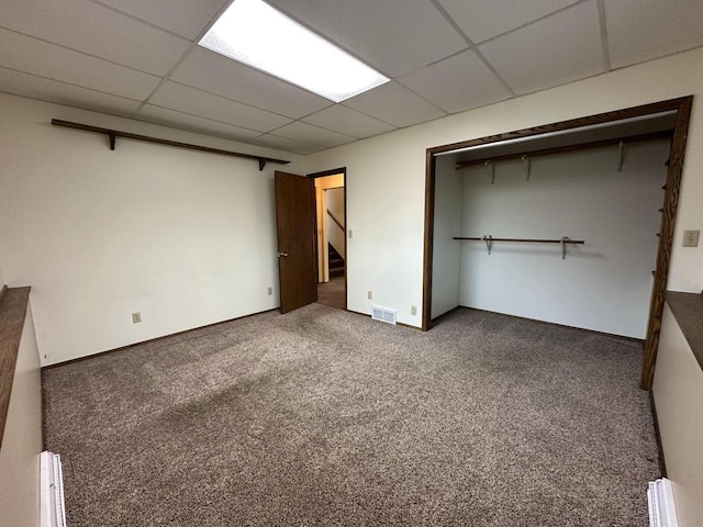 unfurnished bedroom with a paneled ceiling, dark carpet, and a closet