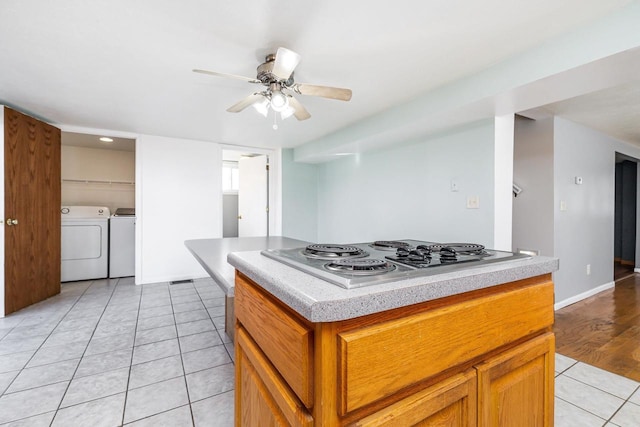 kitchen with ceiling fan, washing machine and dryer, a center island, stainless steel gas cooktop, and light tile patterned flooring