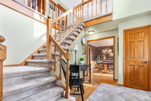 staircase featuring a high ceiling, wood-type flooring, and an inviting chandelier