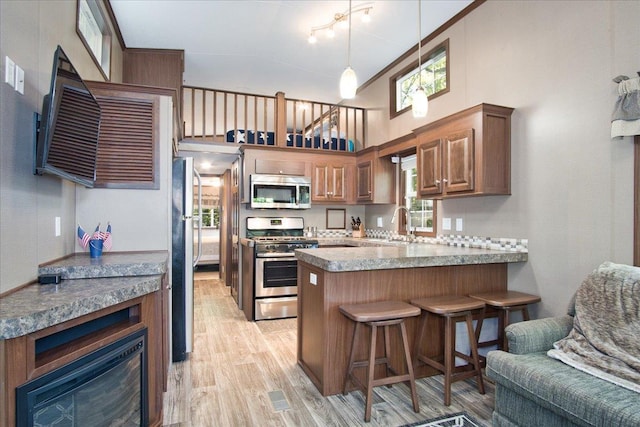 kitchen with a kitchen breakfast bar, kitchen peninsula, stainless steel appliances, light hardwood / wood-style floors, and a high ceiling