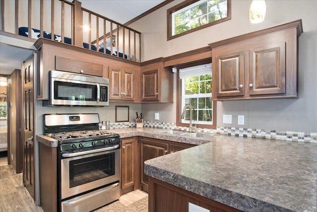 kitchen with sink, crown molding, appliances with stainless steel finishes, a towering ceiling, and light wood-type flooring