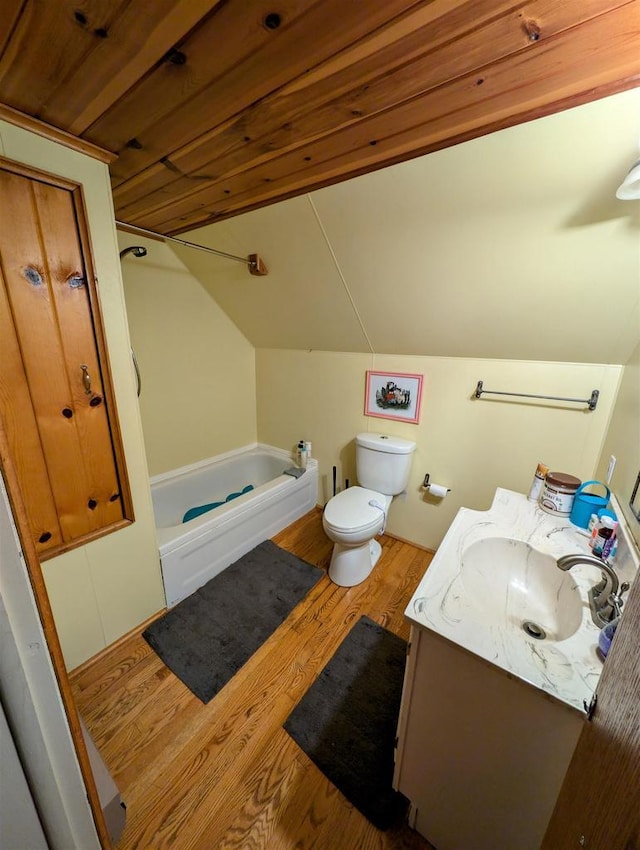 bathroom with lofted ceiling, hardwood / wood-style flooring, a bathing tub, vanity, and toilet