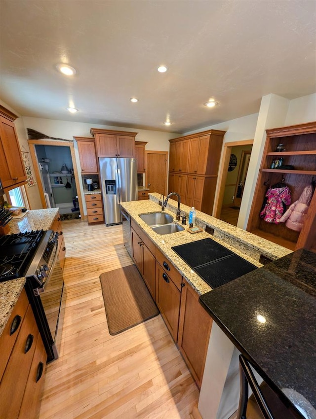 kitchen featuring appliances with stainless steel finishes, light stone countertops, sink, and light hardwood / wood-style flooring