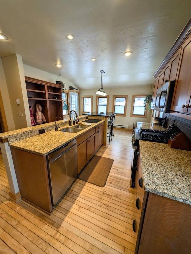 kitchen featuring appliances with stainless steel finishes, pendant lighting, sink, a kitchen island with sink, and light hardwood / wood-style floors