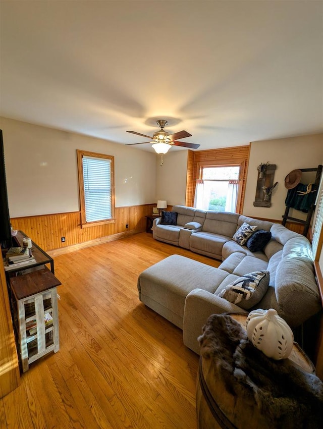 living room featuring ceiling fan, wooden walls, and light wood-type flooring