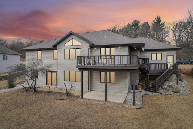 back house at dusk featuring a patio, a deck, and a lawn