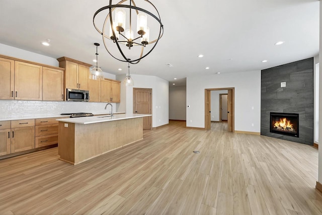 kitchen featuring sink, hanging light fixtures, backsplash, an island with sink, and light wood-type flooring