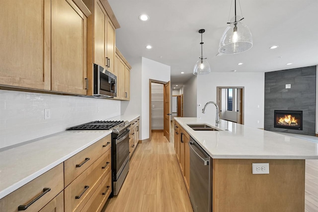 kitchen with appliances with stainless steel finishes, sink, hanging light fixtures, a kitchen island with sink, and light wood-type flooring