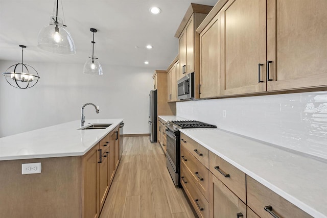 kitchen featuring sink, hanging light fixtures, stainless steel appliances, a kitchen island with sink, and backsplash