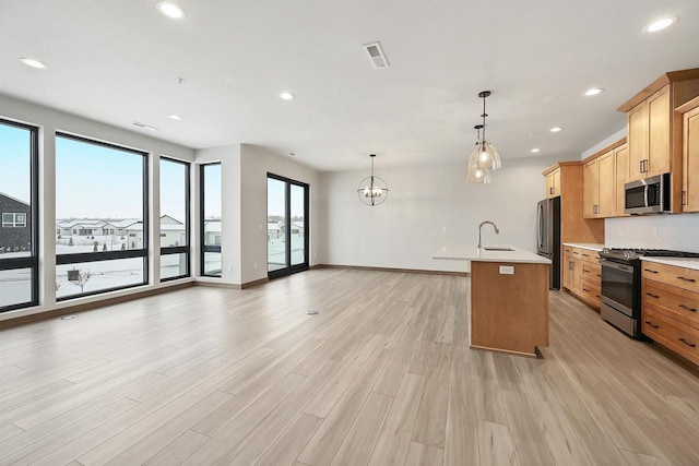 kitchen with sink, decorative light fixtures, light hardwood / wood-style flooring, an island with sink, and stainless steel appliances