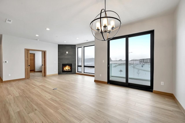 unfurnished living room featuring light hardwood / wood-style flooring, a large fireplace, and a chandelier