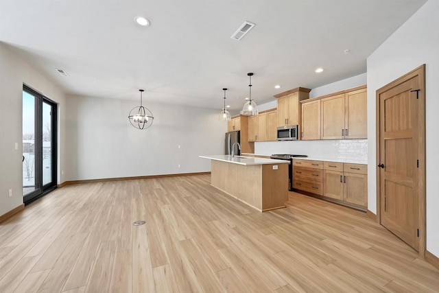 kitchen with sink, light hardwood / wood-style flooring, stainless steel appliances, an island with sink, and decorative light fixtures