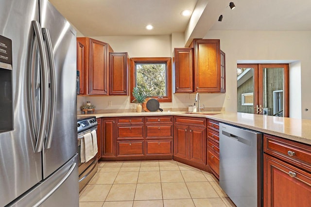 kitchen with sink, light tile patterned floors, appliances with stainless steel finishes, kitchen peninsula, and light stone countertops