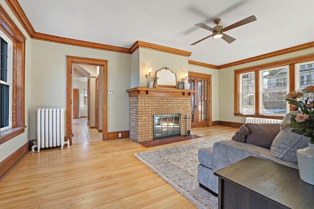 living room with radiator, a fireplace, ornamental molding, and light wood-type flooring