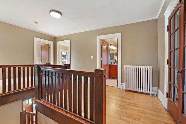 corridor with ornamental molding, radiator heating unit, and light hardwood / wood-style floors