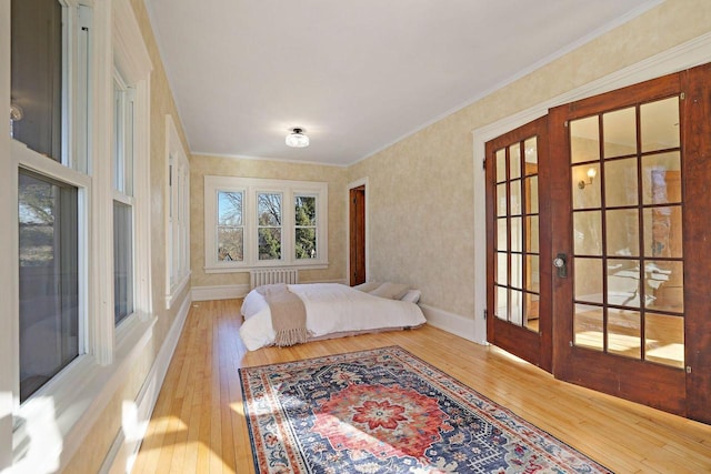 bedroom with radiator heating unit, wood-type flooring, ornamental molding, and french doors