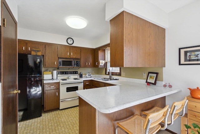 kitchen with sink, black fridge, white range with electric cooktop, a kitchen bar, and kitchen peninsula