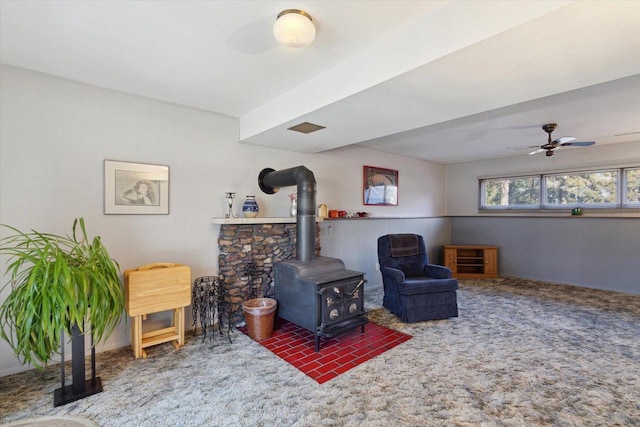 sitting room with carpet floors, ceiling fan, and a wood stove