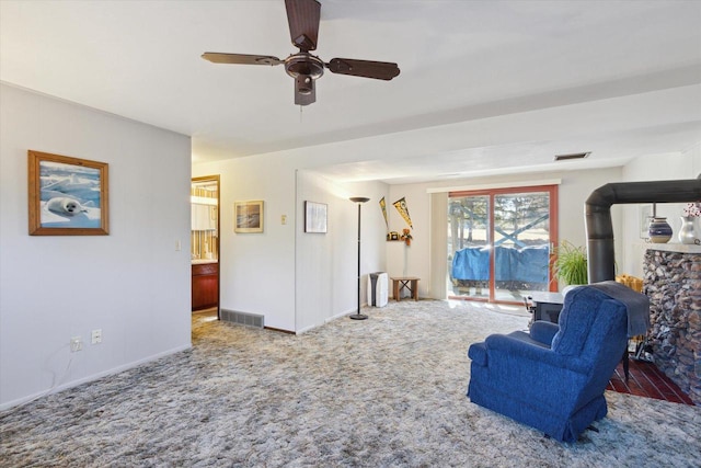 living room with ceiling fan, carpet, and a wood stove