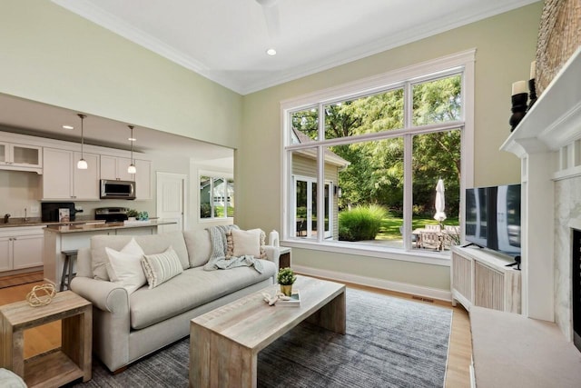 living room with crown molding, a fireplace, a wealth of natural light, and light wood-type flooring