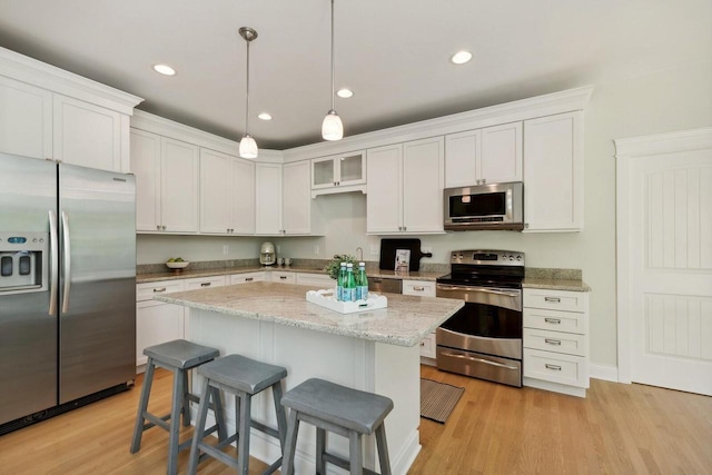 kitchen with appliances with stainless steel finishes, decorative light fixtures, a kitchen island, and white cabinets