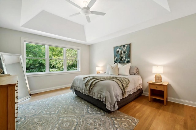 bedroom with a tray ceiling, ceiling fan, and light wood-type flooring