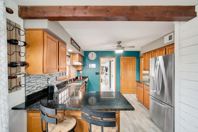 kitchen with beamed ceiling, tasteful backsplash, dark stone countertops, stainless steel fridge, and a kitchen breakfast bar