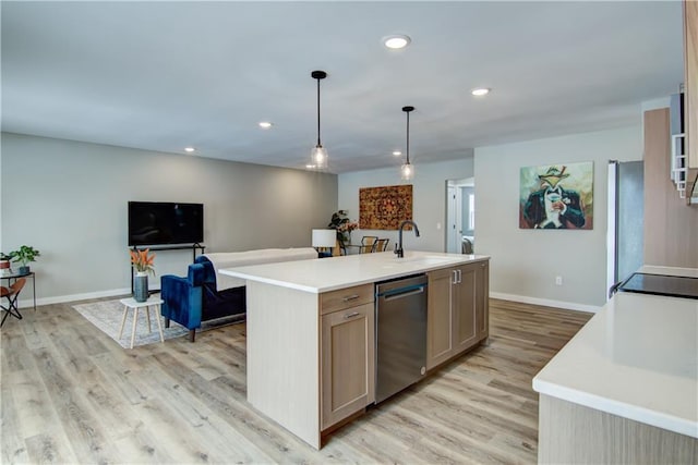 kitchen featuring pendant lighting, sink, stainless steel dishwasher, light hardwood / wood-style floors, and a center island with sink