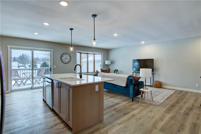 kitchen with sink, hanging light fixtures, a center island with sink, light wood-type flooring, and dishwasher