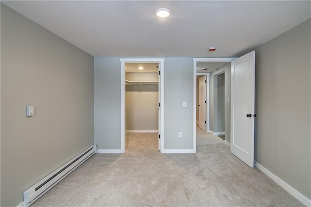 unfurnished bedroom featuring a baseboard radiator, light colored carpet, a closet, and a walk in closet