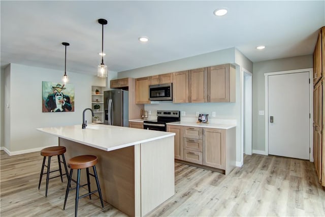 kitchen with sink, hanging light fixtures, light wood-type flooring, an island with sink, and stainless steel appliances