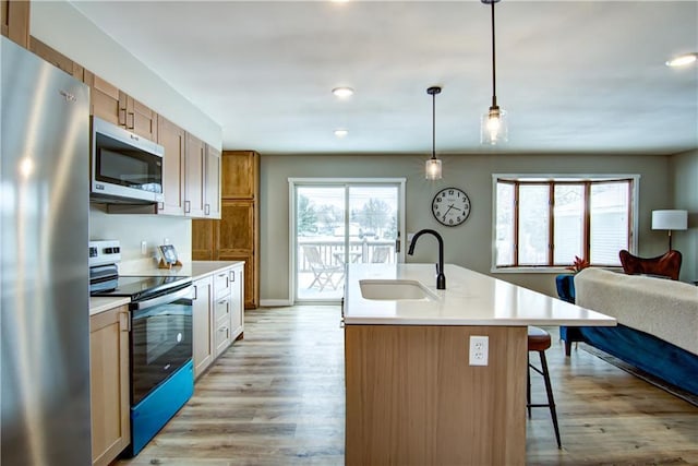 kitchen featuring pendant lighting, sink, a kitchen island with sink, stainless steel appliances, and light hardwood / wood-style floors