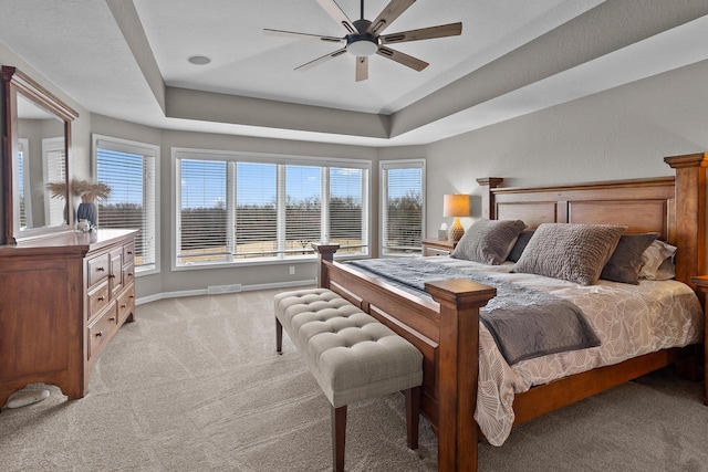 carpeted bedroom with a raised ceiling and ceiling fan