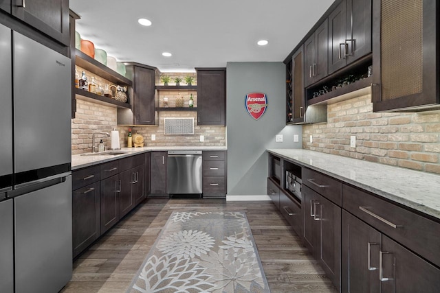 kitchen with sink, dark wood-type flooring, stainless steel appliances, light stone counters, and decorative backsplash