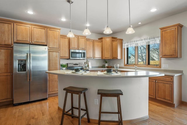 kitchen featuring stainless steel appliances, decorative light fixtures, a center island, and light hardwood / wood-style floors