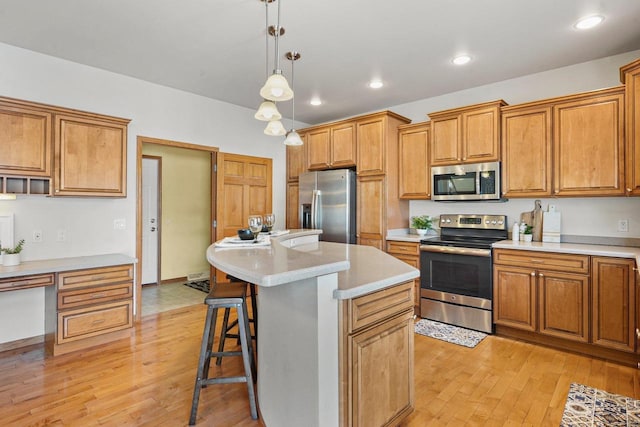 kitchen with a breakfast bar area, hanging light fixtures, stainless steel appliances, a center island, and light hardwood / wood-style floors