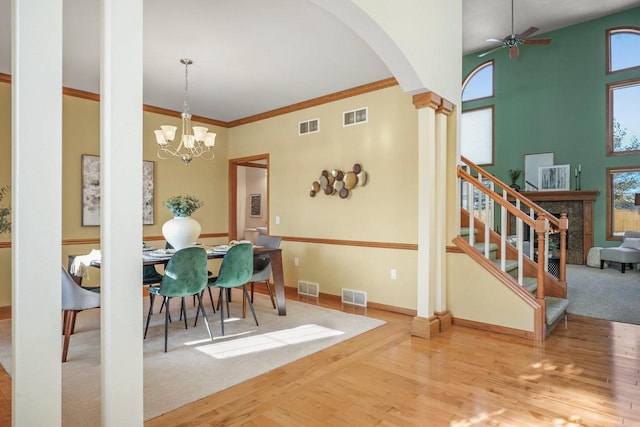 dining room with ornate columns, crown molding, hardwood / wood-style floors, ceiling fan with notable chandelier, and a high ceiling