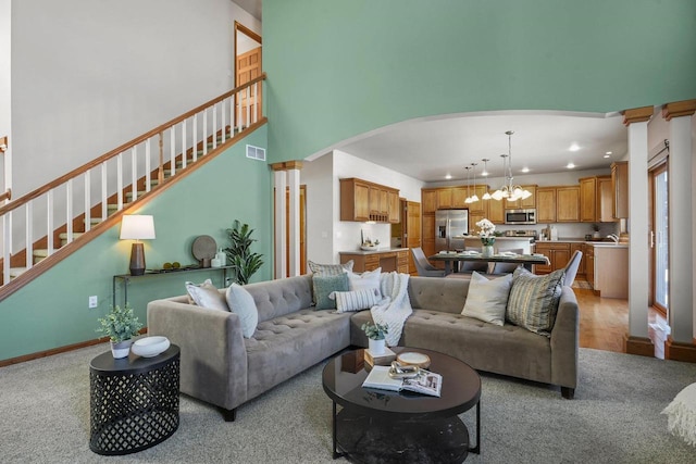 living room featuring an inviting chandelier, light colored carpet, a high ceiling, and ornate columns