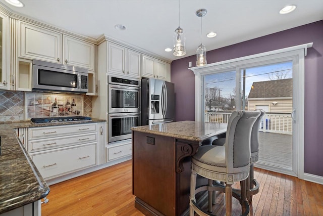 kitchen with backsplash, appliances with stainless steel finishes, decorative light fixtures, and dark stone countertops