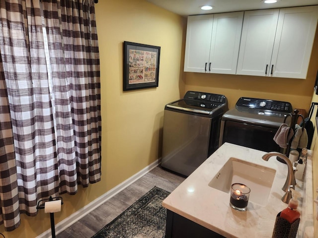 washroom with hardwood / wood-style flooring, cabinets, sink, and washing machine and dryer