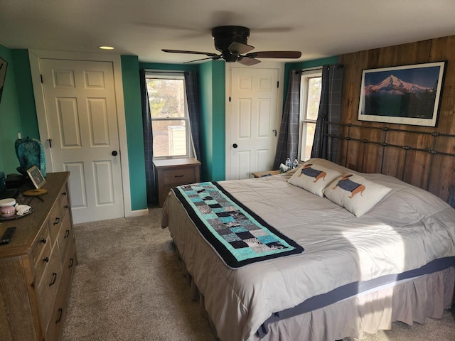 carpeted bedroom with multiple windows, ceiling fan, and wooden walls