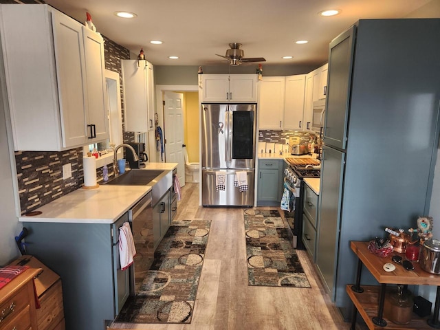 kitchen featuring sink, wood-type flooring, white cabinets, stainless steel appliances, and backsplash