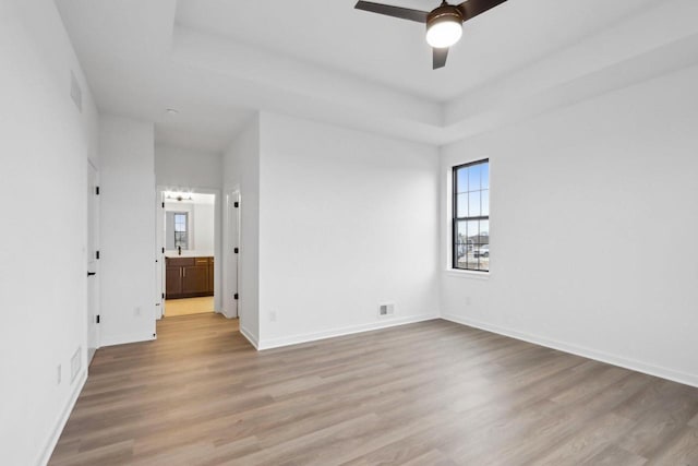 spare room featuring ceiling fan, light hardwood / wood-style floors, and a tray ceiling