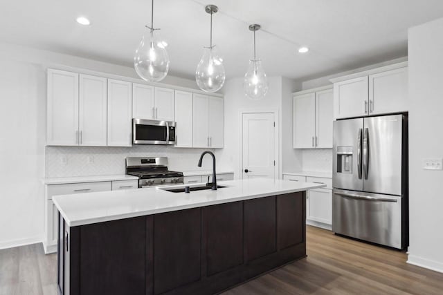 kitchen with appliances with stainless steel finishes, pendant lighting, an island with sink, sink, and white cabinets